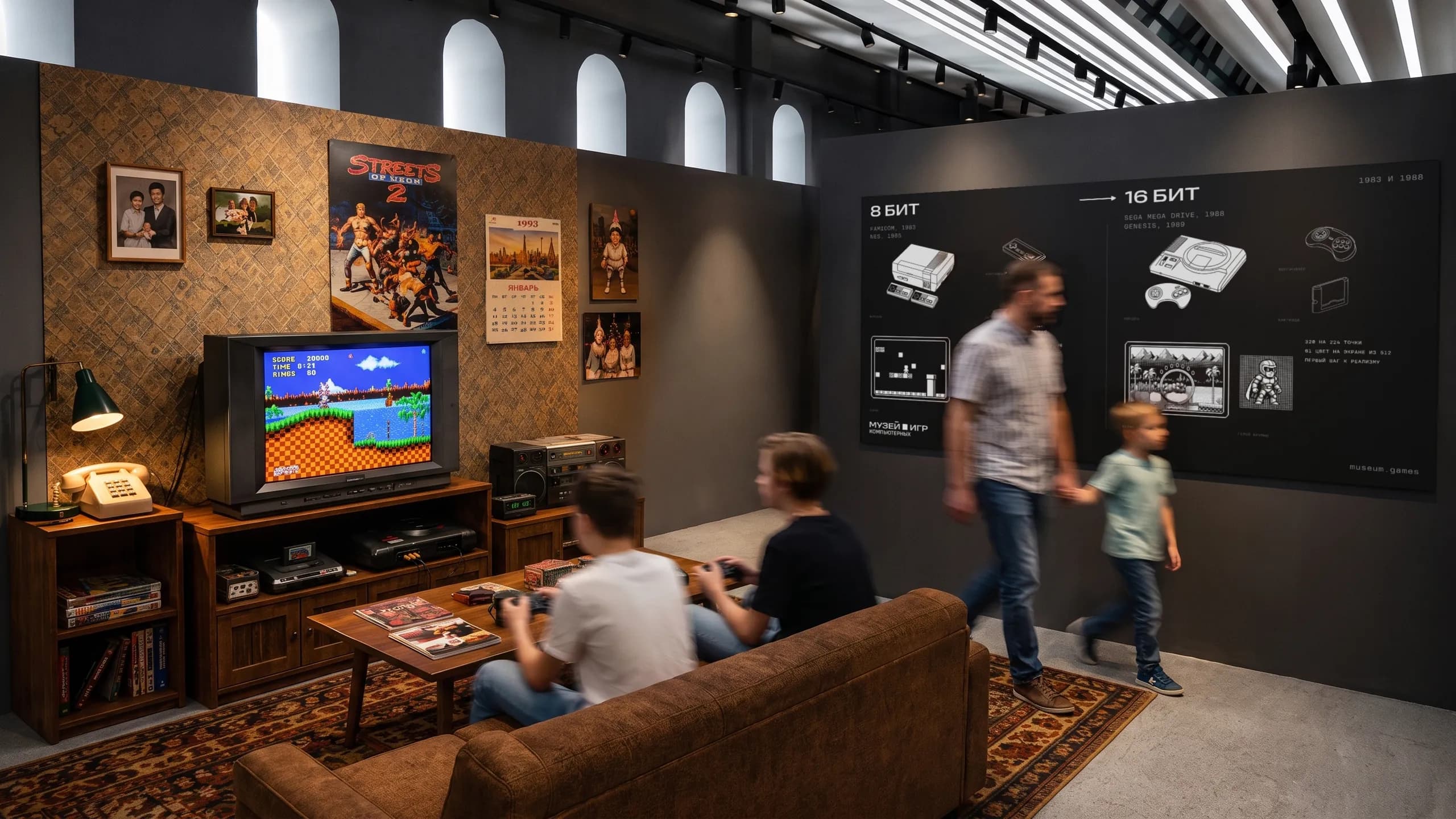 Зал консолей: гостиная девяностых с приставкой Sega у телевизора, на диване играют двое, рядом щит «8 бит, 16 бит».