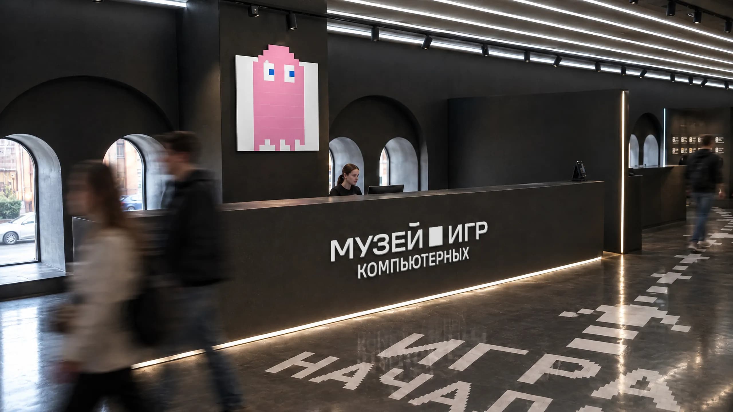 The museum reception: a desk with the Museum of Computer Games sign, a pink pixel ghost on the wall and the words "The game has begun" on the floor.
